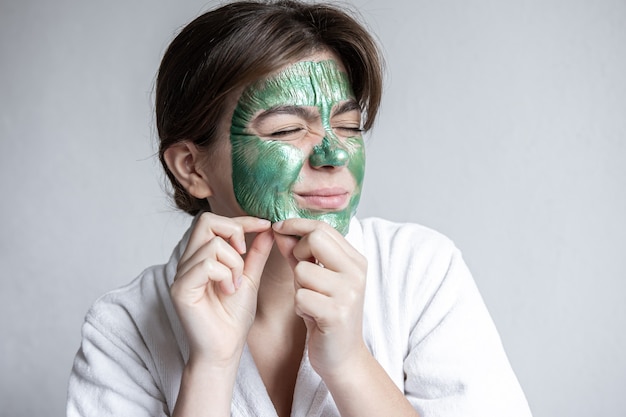 Jonge vrouw verwijdert groen masker van gezicht, collageenmasker voor gezichtshuid, spa-procedure.