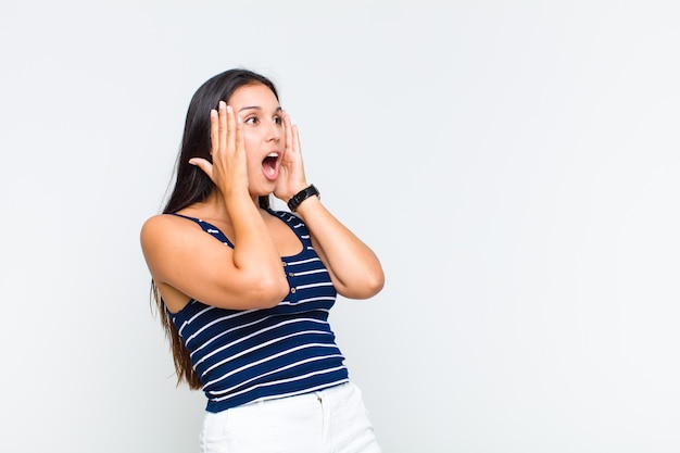 Jonge vrouw voelt zich blij, opgewonden en verrast, naar de zijkant kijkend met beide handen op het gezicht