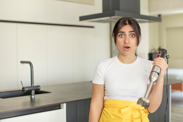 jonge vrouw voelt zich extreem geschokt en verrast chef-kok met staafmixer