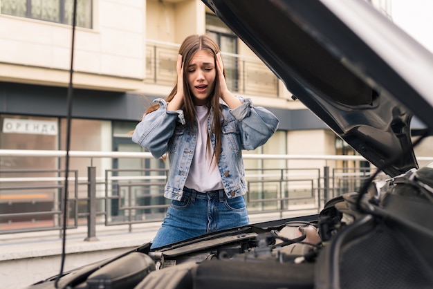 Jonge vrouw wacht op hulp in de buurt van haar auto met pech langs de weg.