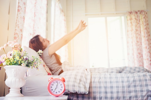 jonge vrouw wakker stretch op het bed in de ochtend wekker ziet er zo fris dag