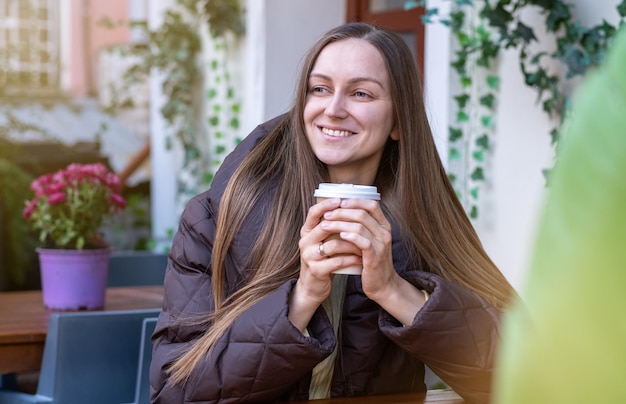 Jonge vrouw warmt op met een kopje koffie op straat bij koud weer een jonge blonde glimlachende blanke jonge vrouw