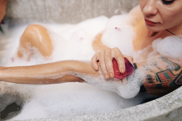 Jonge vrouw wast haar lichaam met geparfumeerde zeep wanneer ze ontspant in bubbelbad