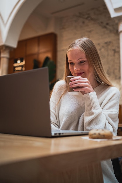 Jonge vrouw werkt hard met haar computer terwijl ze een kopje koffie drinkt in een cafetaria