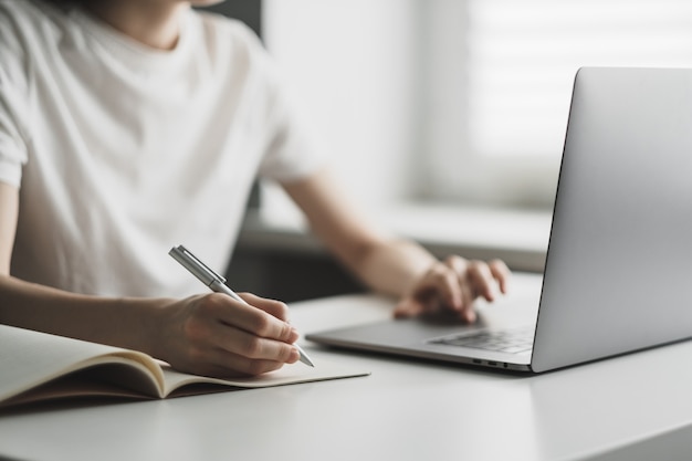 Jonge vrouw werkt op een laptop en maakt aantekeningen in een notitieblok