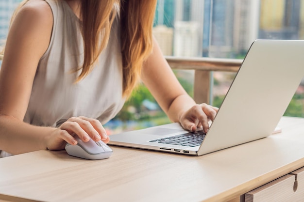 Jonge vrouw werkt op een laptop op haar balkon met uitzicht op de wolkenkrabbers. freelancer, werken op afstand, thuiswerken