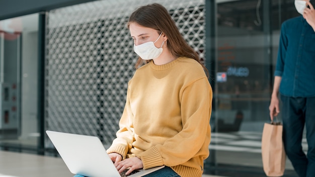 Jonge vrouw werkt op een laptop terwijl ze buiten een stadsgebouw zit