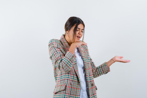 Jonge vrouw wijst iets met geopende handpalmen op witte achtergrond