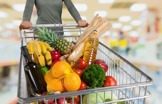 Jonge vrouw winkelen in de winkel met winkelwagentje met portemonnee in handen