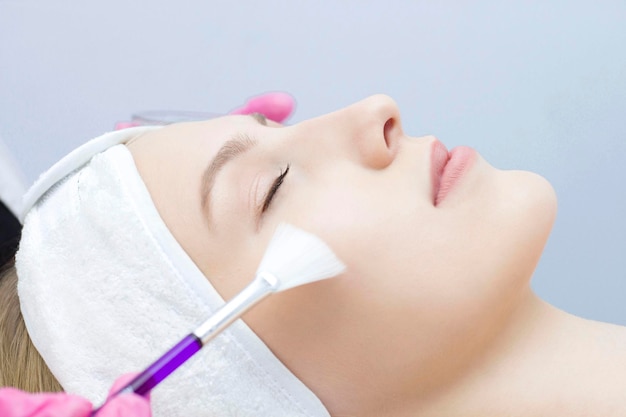 Jonge vrouw wordt met een borstel op het masker op het gezicht aangebracht Procedure bij de schoonheidsspecialist Relax