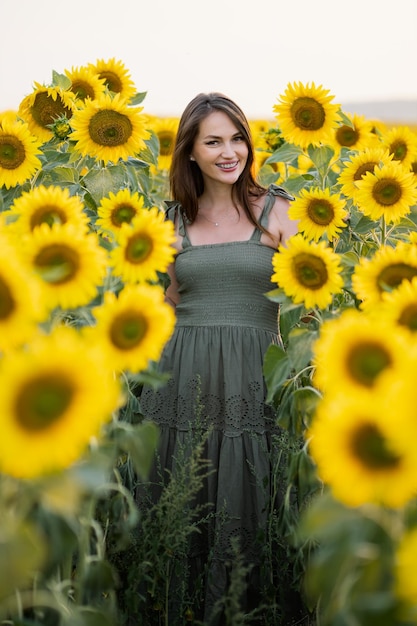 Jonge vrouw ziet er glimlachend uit terwijl ze tegen het zonnebloemveld staat