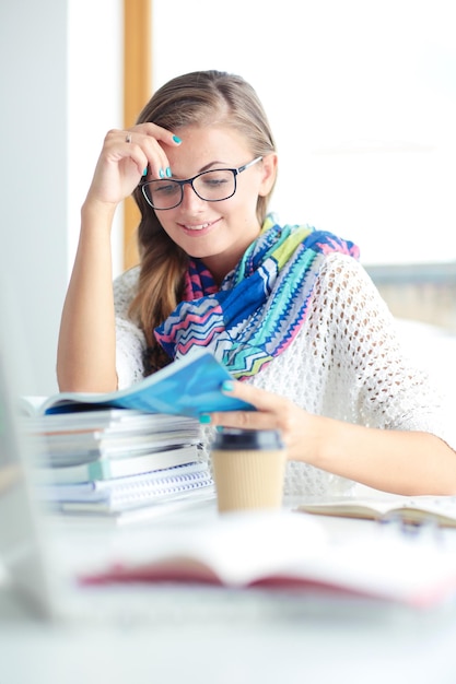 Jonge vrouw zit aan een bureau tussen boeken Student