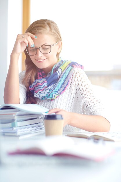 Jonge vrouw zit aan een bureau tussen boeken Student