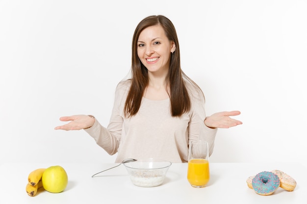 Jonge vrouw zit aan tafel ontbijt met granen en melk, jus d'orange in glas, donuts geïsoleerd op een witte achtergrond. Goede voeding, heerlijk lekker eten, gezonde levensstijl. Gebied om ruimte te kopiëren.