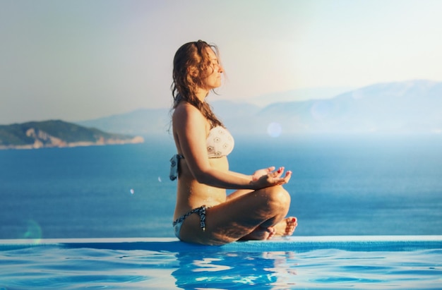 Jonge vrouw zit bij een infinity pool bij de zee tegen de lucht