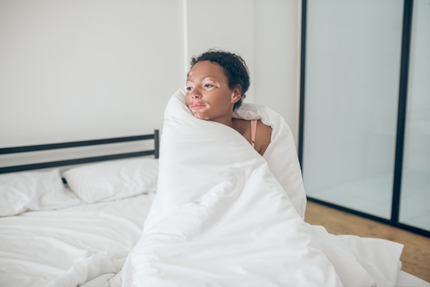 Jonge vrouw zit in bed bedekt met deken en voelt zich ontspannen feeling