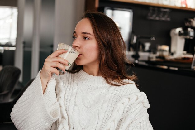 Foto jonge vrouw zit in café en drinkt koffie binnenshuis kaukasisch meisje in trui