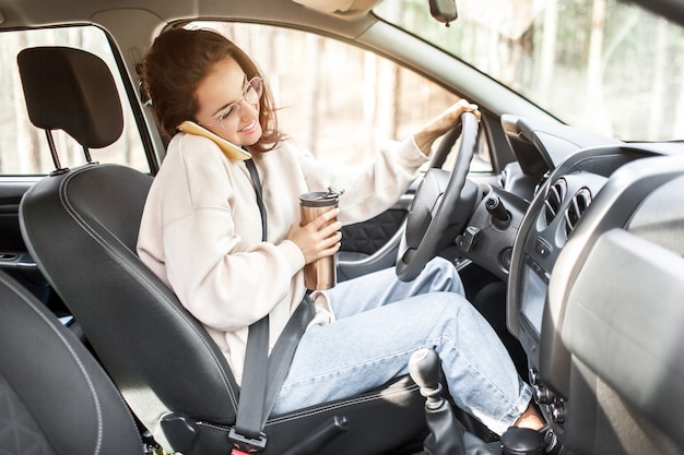 Jonge vrouw zit in een auto. Het mooie donkerbruine model gebruikt een smartphone of telefoon