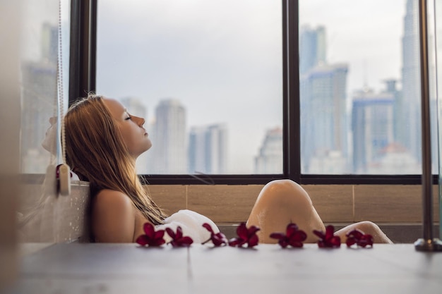 Jonge vrouw zit in een bad met schuim en frangipani bloemen tegen de achtergrond van een panoramisch