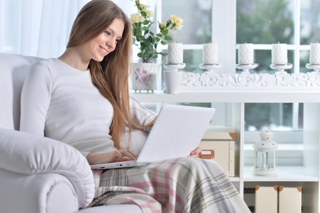 Jonge vrouw zit in een fauteuil met behulp van laptop