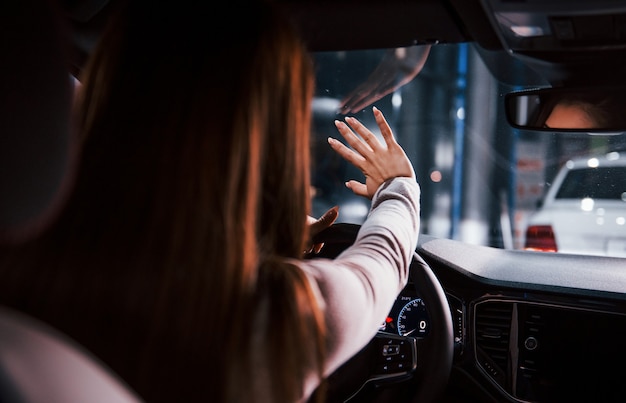 Jonge vrouw zit in een gloednieuwe moderne auto die haar hand vasthoudt.