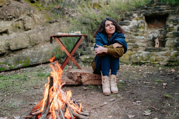 Jonge vrouw zit naast een vuur tijdens een winterpicknick.