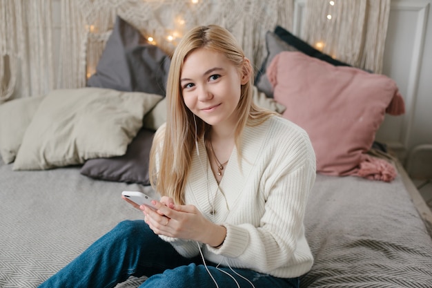 Jonge vrouw zit op bed en maakt gebruik van een smartphone