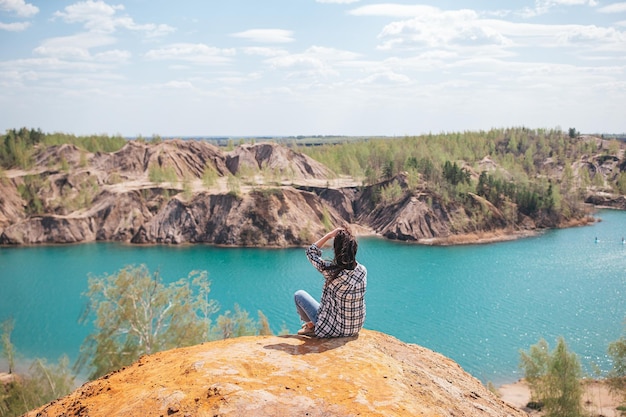 Foto jonge vrouw zit op de top van de berg en voelt zich vrij en kijkt naar het blauwe meer