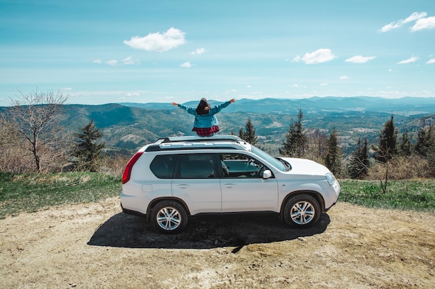 Jonge vrouw zit op de top van de suv-auto op de bergtop en geniet van het uitzicht op het landschap