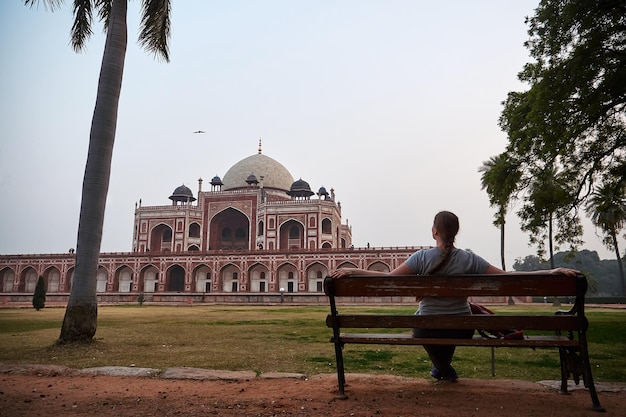 Jonge vrouw zit op een bankje en kijkt naar Humayun-graf Mughal-keizer in Delhi, India