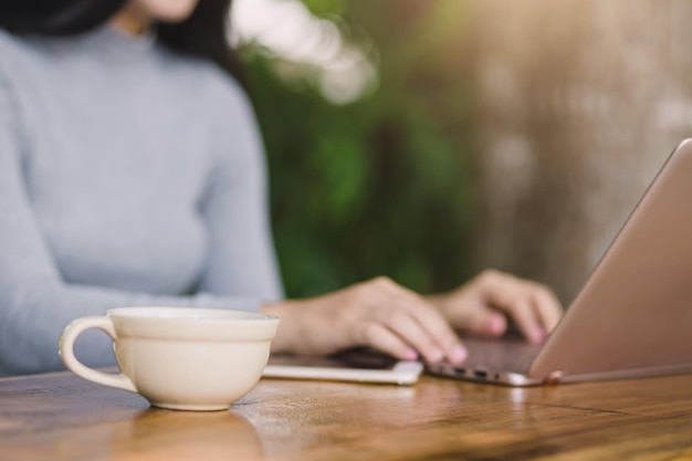 Jonge vrouw zitten in coffeeshop aan houten tafel koffie drinken en laptop gebruiken