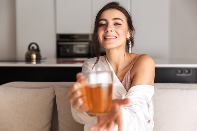 jonge vrouw zitten in de keuken, glas met thee te houden