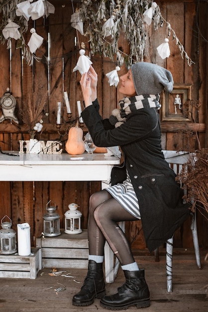 Jonge vrouw zittend aan tafel op het terras van een oud houten huis versierd met pompoenen tijdens halloween