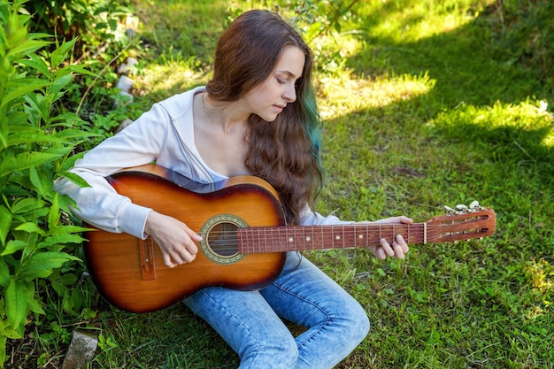 Jonge vrouw zittend in het gras en gitaar spelen