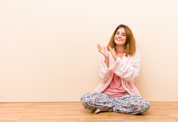 Jonge vrouw, zittend om thuis te zitten pyjama's voelen zich gelukkig en succesvol, glimlachen en klappen handen, zeggen gefeliciteerd met een applaus