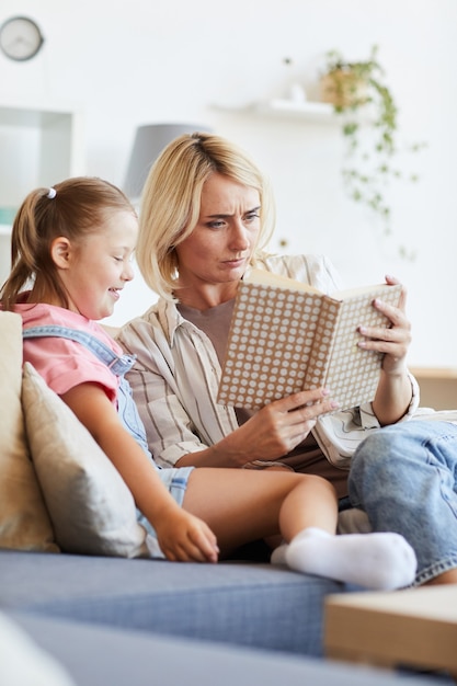 Jonge vrouw zittend op de bank en het lezen van een boek voor meisje met het syndroom van Down in de kamer