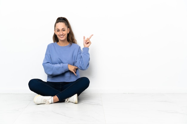 Jonge vrouw zittend op de vloer blij en omhoog