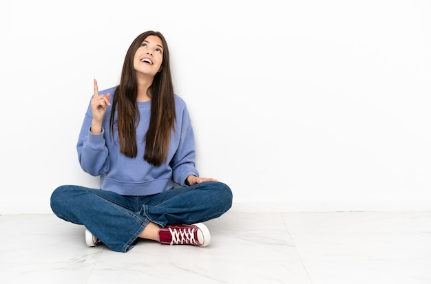 Jonge vrouw zittend op de vloer die naar boven wijst en verrast?