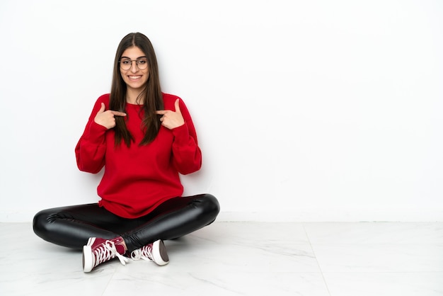 Jonge vrouw zittend op de vloer geïsoleerd op een witte achtergrond met verrassing gezichtsuitdrukking