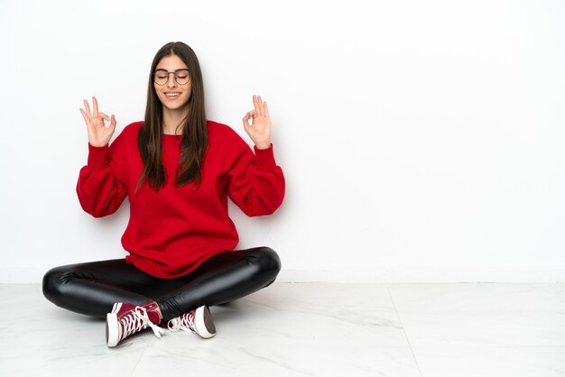 Jonge vrouw zittend op de vloer geïsoleerd op een witte muur in zen pose