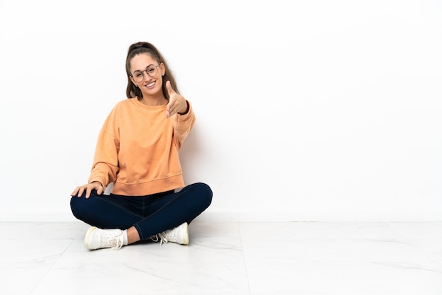 Jonge vrouw zittend op de vloer handen schudden voor het sluiten van een goede deal