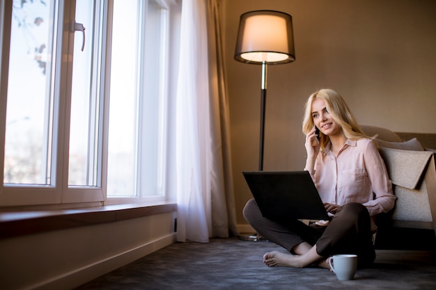 Jonge vrouw zittend op de vloer in de kamer met laptop