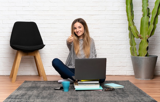 Jonge vrouw zittend op de vloer met haar laptop handshaking na goede deal