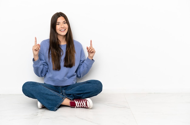 Jonge vrouw zittend op de vloer wijzend op een geweldig idee