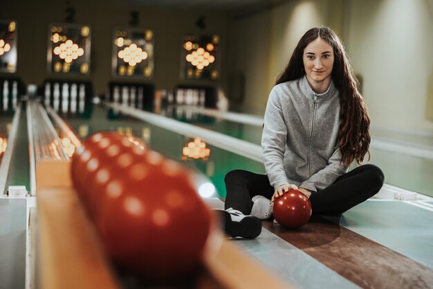 Jonge vrouw zittend op een baan met een bowlingbal terwijl ze zich voorbereidt op het gooien naar de bowlingclub.