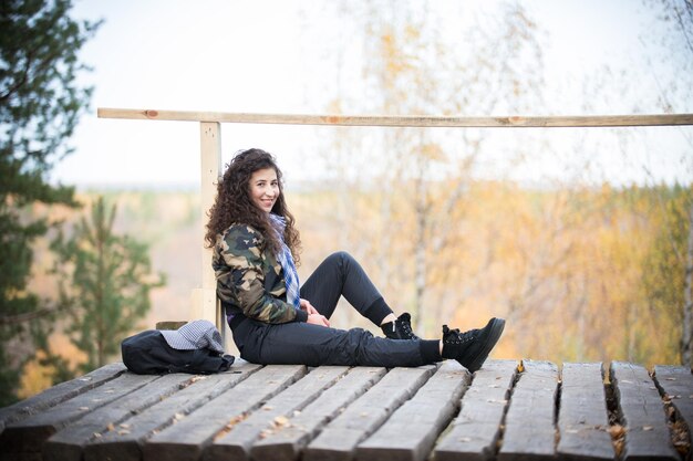 Jonge vrouw zittend op een platform op een achtergrond van het bos glimlachend