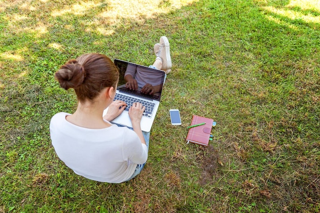 Jonge vrouw zittend op groen gras gazon in stadspark bezig met laptop pc-computer. Freelance bedrijfsconcept