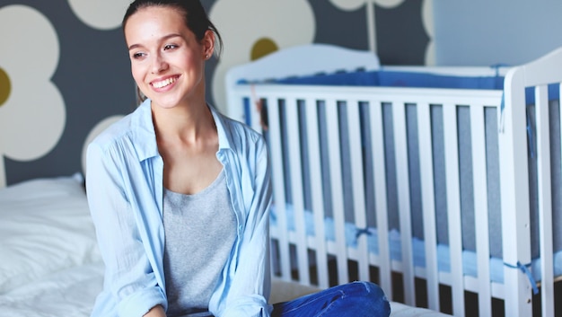 Jonge vrouw zittend op het bed in de buurt van kinderbedje Jonge moeder