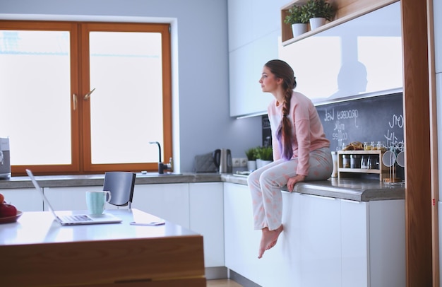 Jonge vrouw zittend op tafel in de keuken