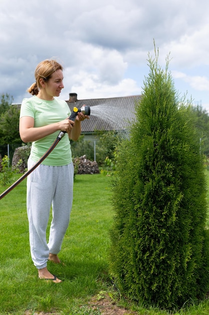 Jonge vrouw zorgt voor naaldplanten in de tuin die ze afwerkt met water uit een slang